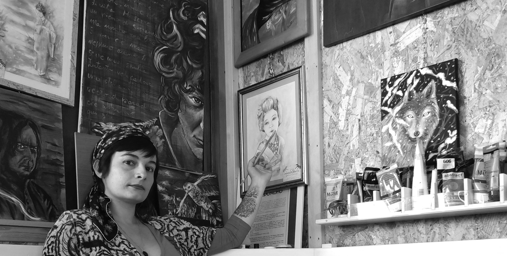 La pittrice seduta nel suo studio tra i quadri. Si notano sullo sfondo un dipinto che ritrae Severus Piton da Harry Potte, un ritratto di Ermal Meta con le parole di una canzone e un acquarello con una donna giapponese in kimono e il ritratto di un lupo tra i rami innevati. Allineati su un lato anche alcuni tubetti di colore.